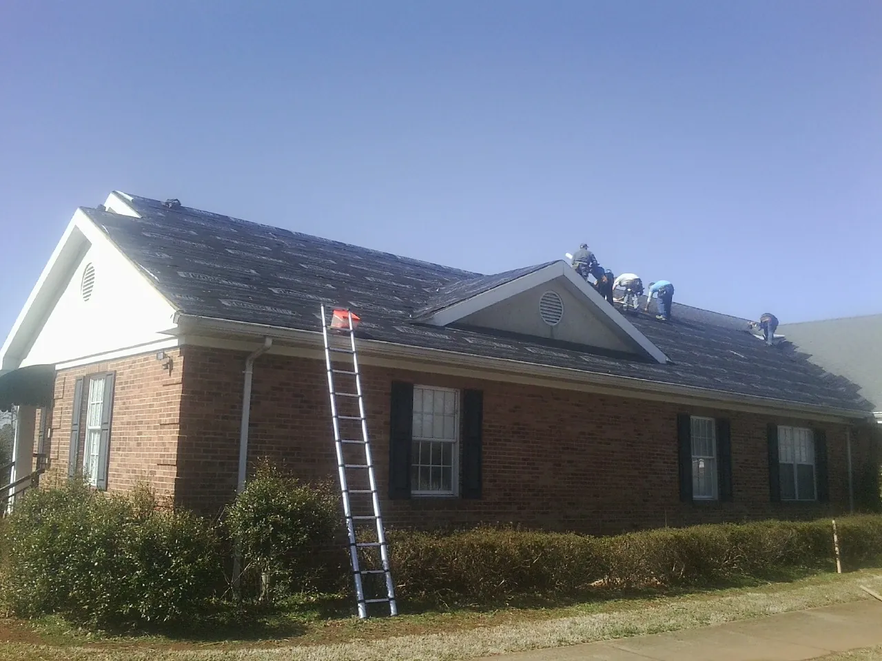 Crew tearing shingles off a brick ranch roof with a ladder set — Metal Roof Repair work by our crew in Central