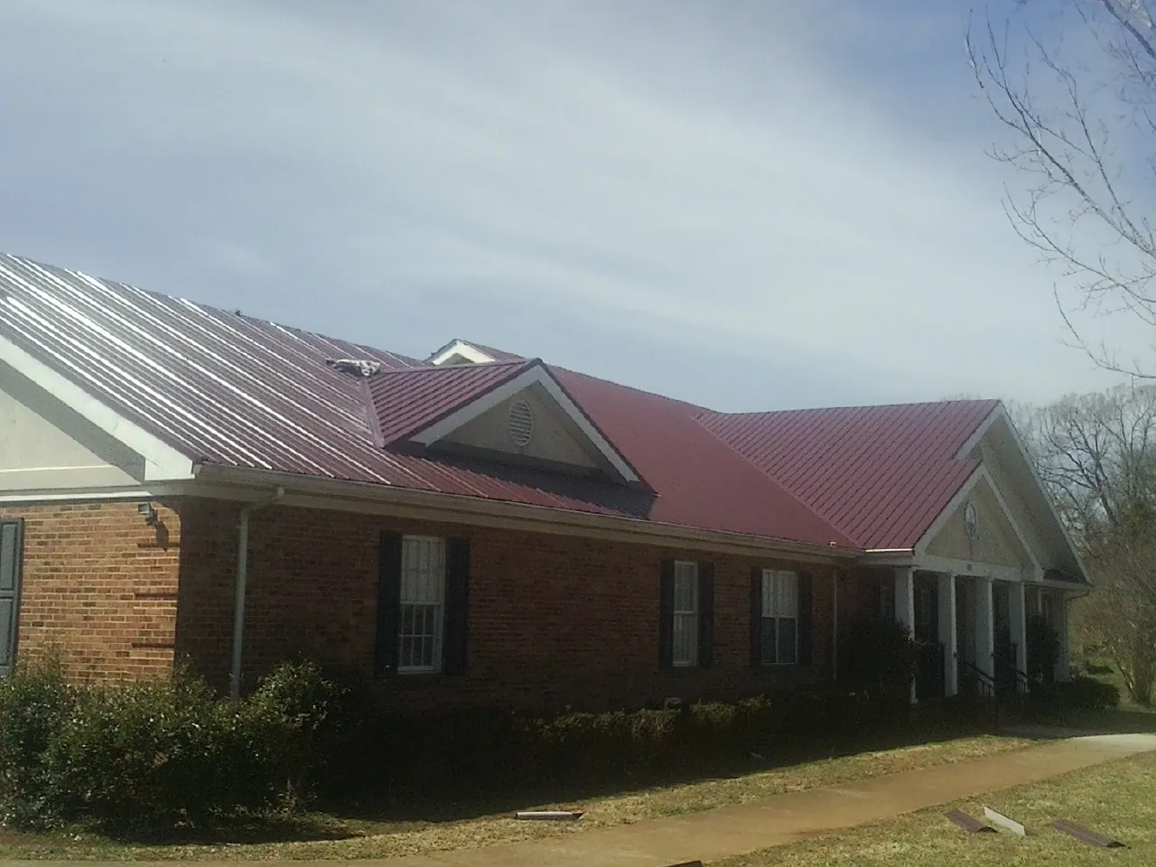 Red metal roof with gabled entries on a long brick building, from a Hail Damage Roof Repair job in Central